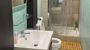 A modern bathroom with a white sink, a toilet, a glass shower enclosure, and a mirror. - Renovated apartment - near beach (Dinard)
