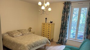A bedroom with a bed, a dresser, a chair, and a window with curtains. - Renovated apartment - near beach (Dinard)