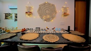 Un espace repas avec une table centrale entourée de chaises, agrémenté de sets de table en fibres tressées et d’une grande décoration murale circulaire.