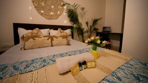 Una cama bien hecha con una colcha estampada, un adorno en la pared, una mesita de noche con un ordenador portátil y un jarrón con flores.