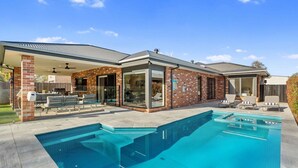 Une maison moderne dotée d’une piscine, d’un patio couvert et d’une façade en briques.