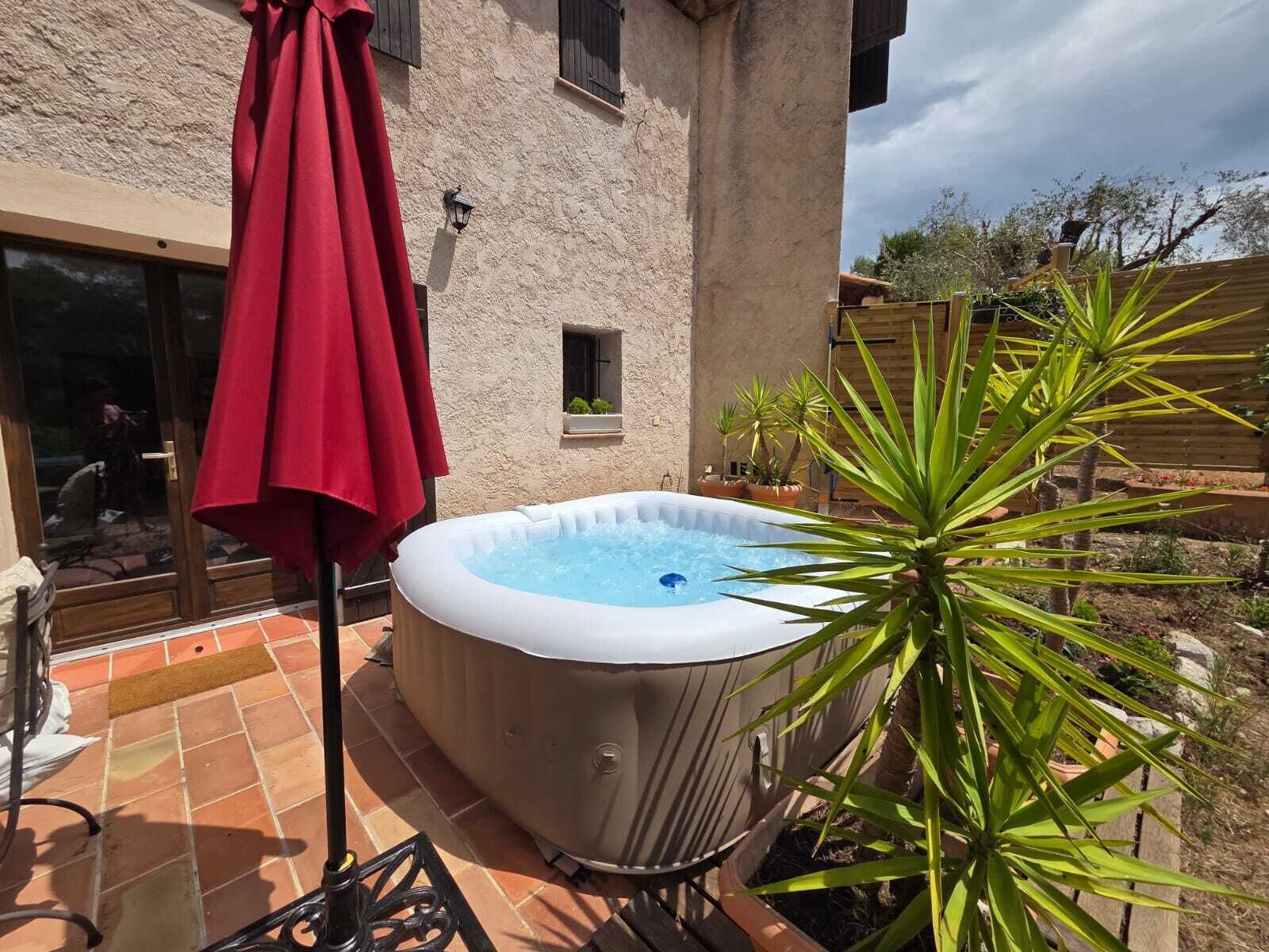Una vasca idromassaggio in giardino, con un ombrello rosso, una finestra piccola e una pianta in vaso.