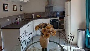 A modern kitchen with white cabinets, a stainless steel sink, and a built-in oven. There is a vase with flowers on the dining table.