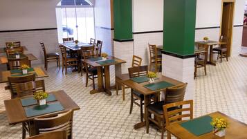 Un restaurante con varias mesas y sillas de madera, individuales verdes y pequeños arreglos florales.