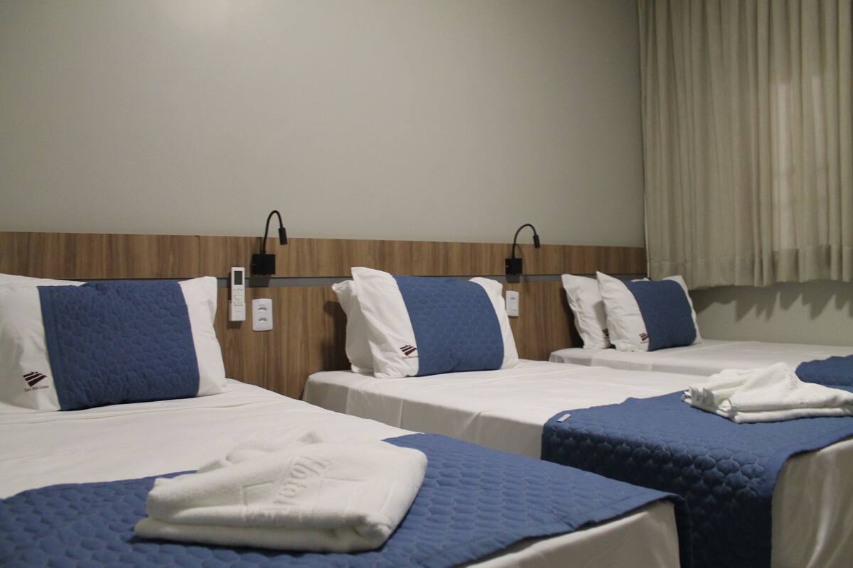Ett hotellrum med tre separata sängar, var och en med ett blått täcke och vita kuddar.