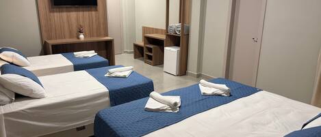 A hotel room with three beds, a TV mounted on the wall, a mirror, and a wardrobe.