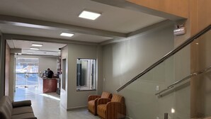 A modern lobby with a reception desk, a seating area with chairs, a glass elevator, and a staircase. - Hotel Mato Grosso Inn (Cuiabá)