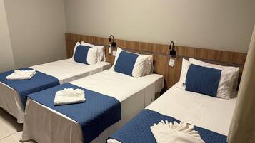 A hotel room with three single beds, each with a blue quilt and white bedding.