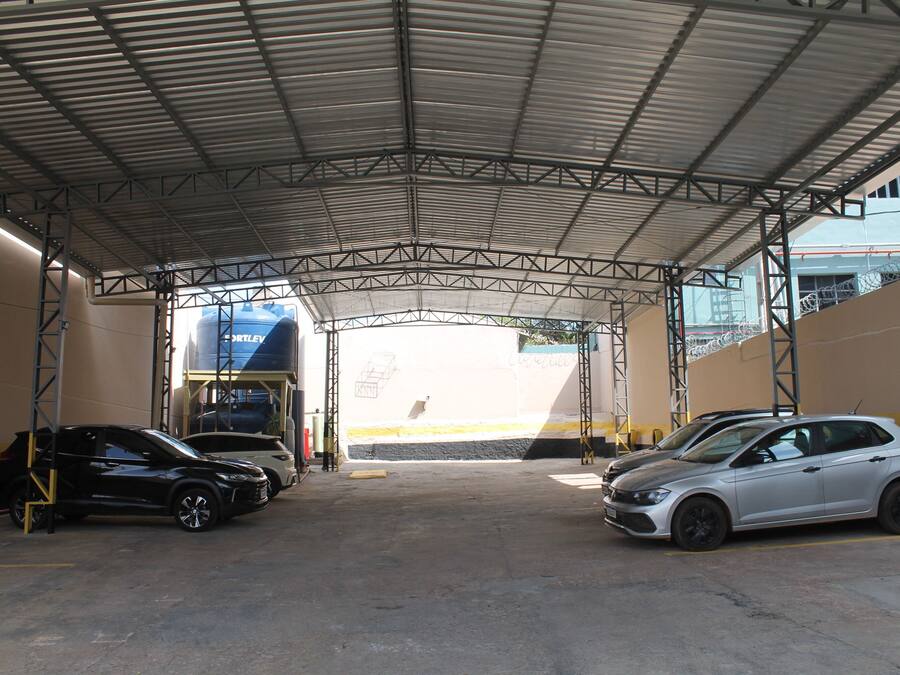 A covered parking area with two cars parked, metal beams, and a large blue structure in the background.