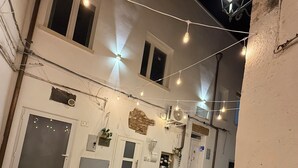 Une cour décorée de guirlandes lumineuses, un bâtiment blanc avec de nombreuses portes et des plantes en pot.