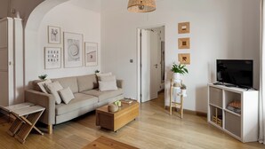 Un salon moderne avec un canapé, une table basse et un meuble pour la télévision. Des tableaux encadrés ornent le mur, et un luminaire suspendu en osier complète l’ensemble.