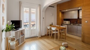 Un salon moderne doté d’un téléviseur à écran plat, d’un coin repas avec une table et des chaises en bois, et d’une cuisine avec des meubles en bois et un four à micro-ondes.