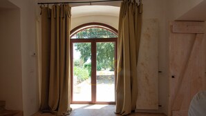 A room with a large arched doorway, beige curtains, a wooden door, and a view of greenery outside.