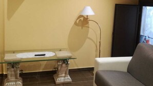 Een woonkamer met een bank, een salontafel met glazen blad, een lamp en een flatscreen televisie die aan de muur is bevestigd.