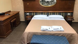 Een hotelkamer met een groot bed, een houten bureau, een stoel, een nachtkastje en een bijzettafeltje.