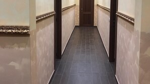 Een gang met donkere betegelde vloer, crèmekleurige muren en decoratieve sierlijsten.