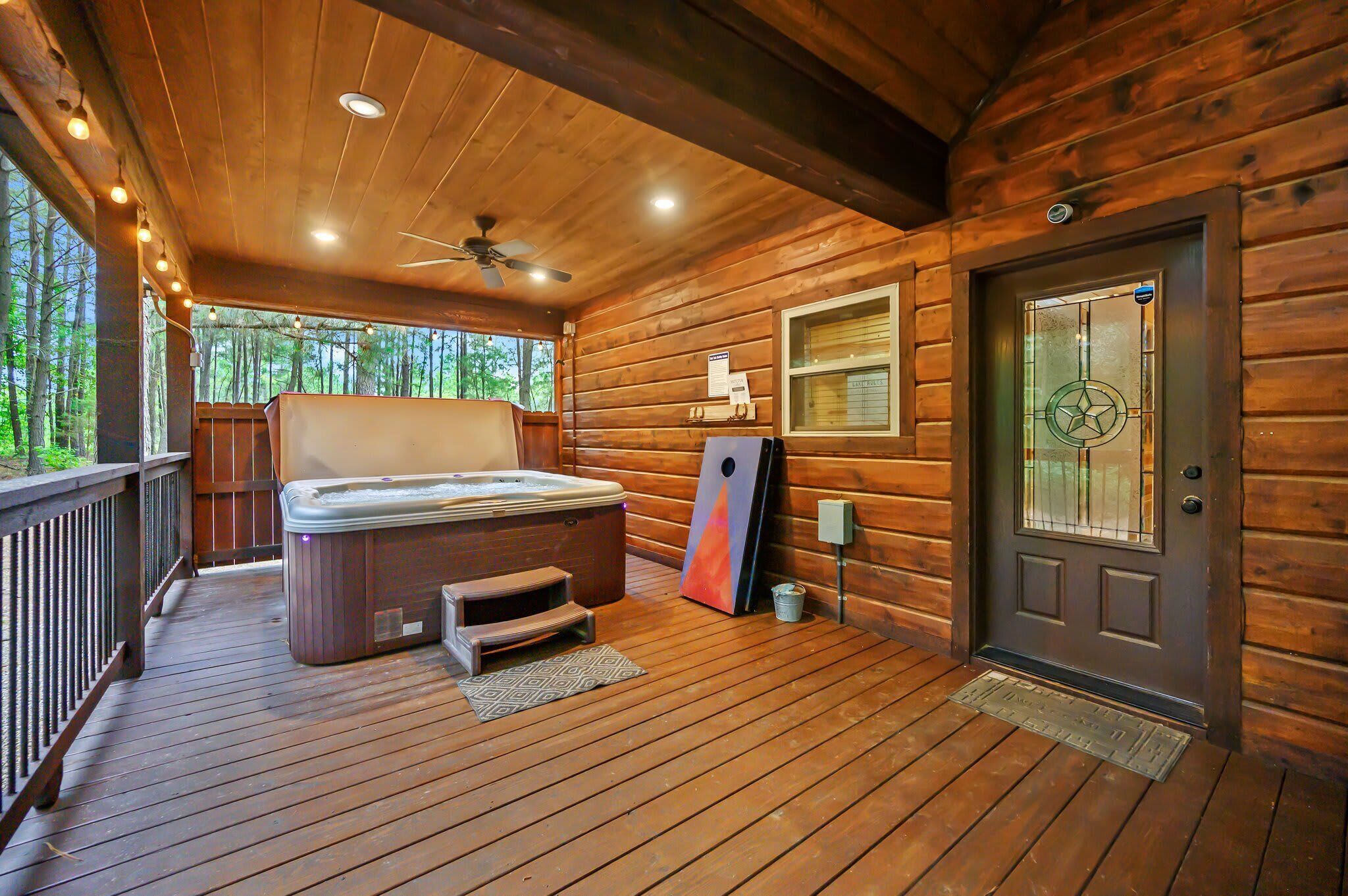 Una cabaña de madera con un jacuzzi, una puerta con panel de vidrio y un ventilador de techo.