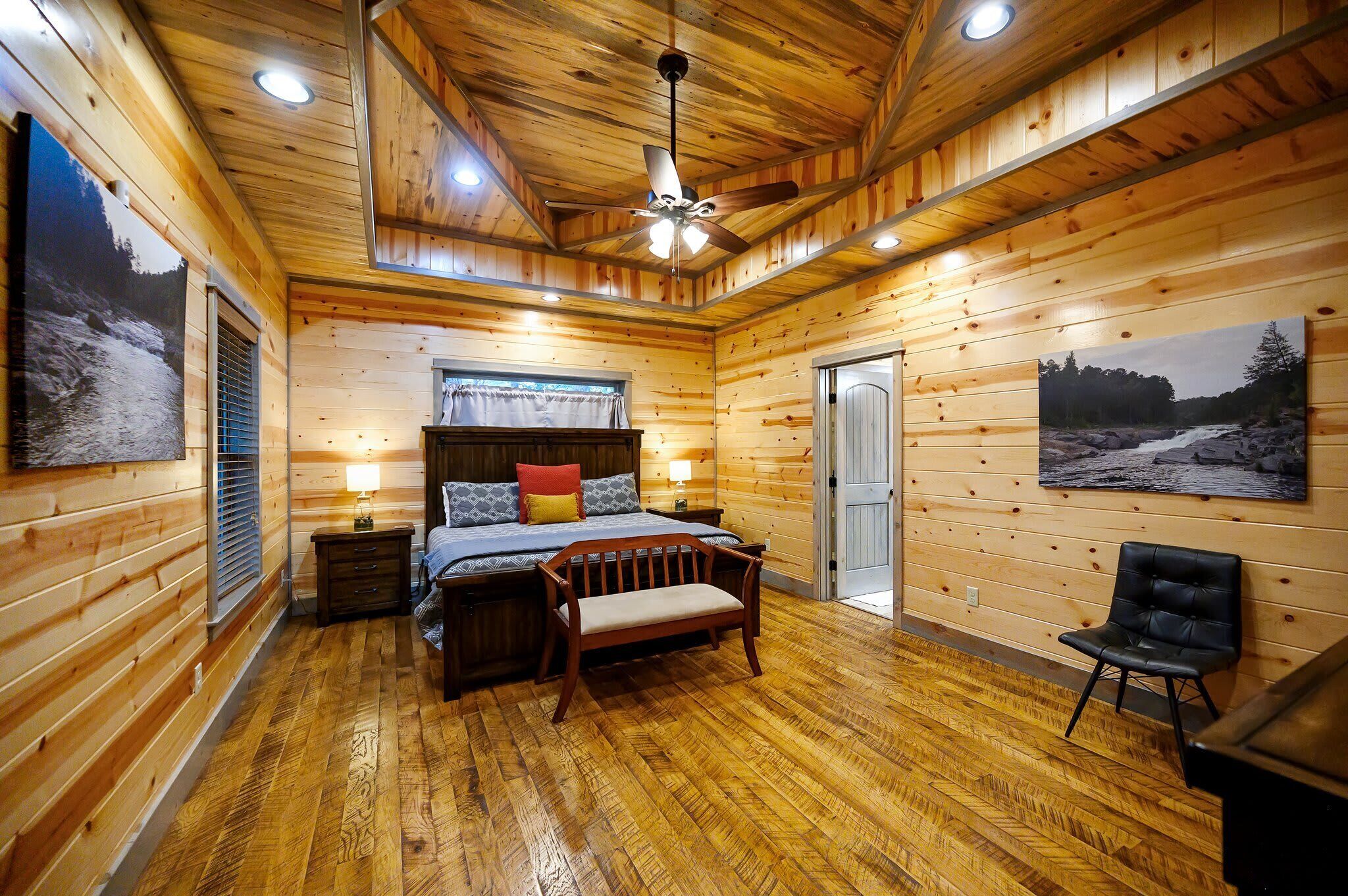 A wooden-paneled bedroom with a bed, bedside table, bench, and a chair.