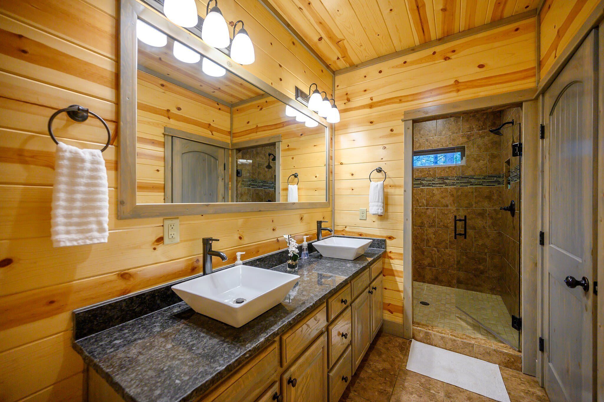 Une salle de bain rustique, avec deux lavabos, un grand miroir et une douche à l’italienne.