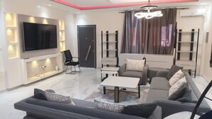 A modern living room with a flat-screen TV, a sofa set, a coffee table, and a bookshelf.