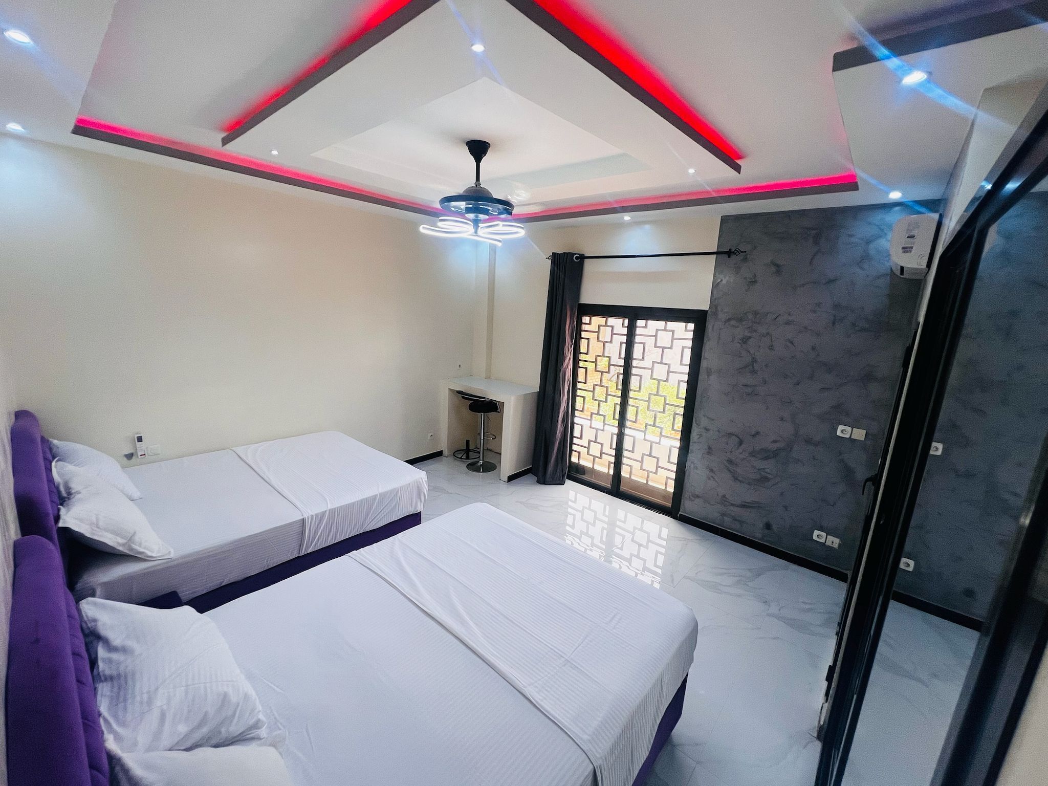 A modern bedroom with two beds, a desk, and a ceiling fan.