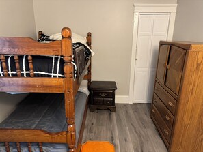 Un dormitorio con cama de madera, una mesita de noche pequeña, un aparador y una puerta.