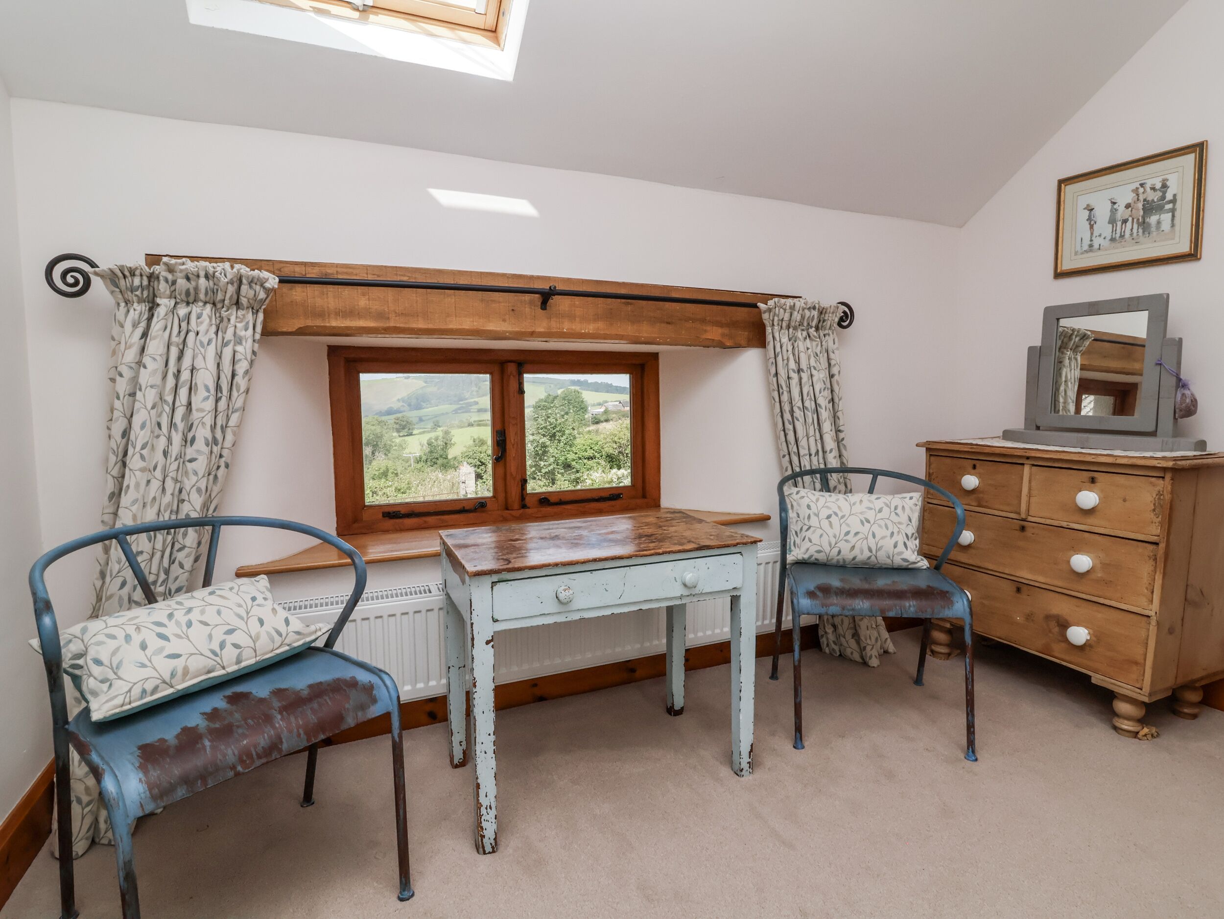 A room with a wooden table, two chairs, a dresser, a window with a view, and a skylight.