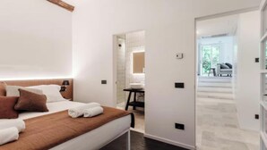 A modern hotel room with a neatly made bed, a bathroom with a large mirror, and a view of the outdoor seating area. - Elegant Apartment in the Heart of Bellagio (Bellagio)