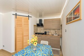 A compact kitchen with a built-in stove, a sink, and a microwave. There's a wooden door and a white chair.