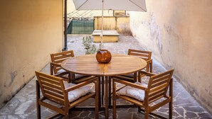 A round wooden table with four chairs, a vase, and a large umbrella.