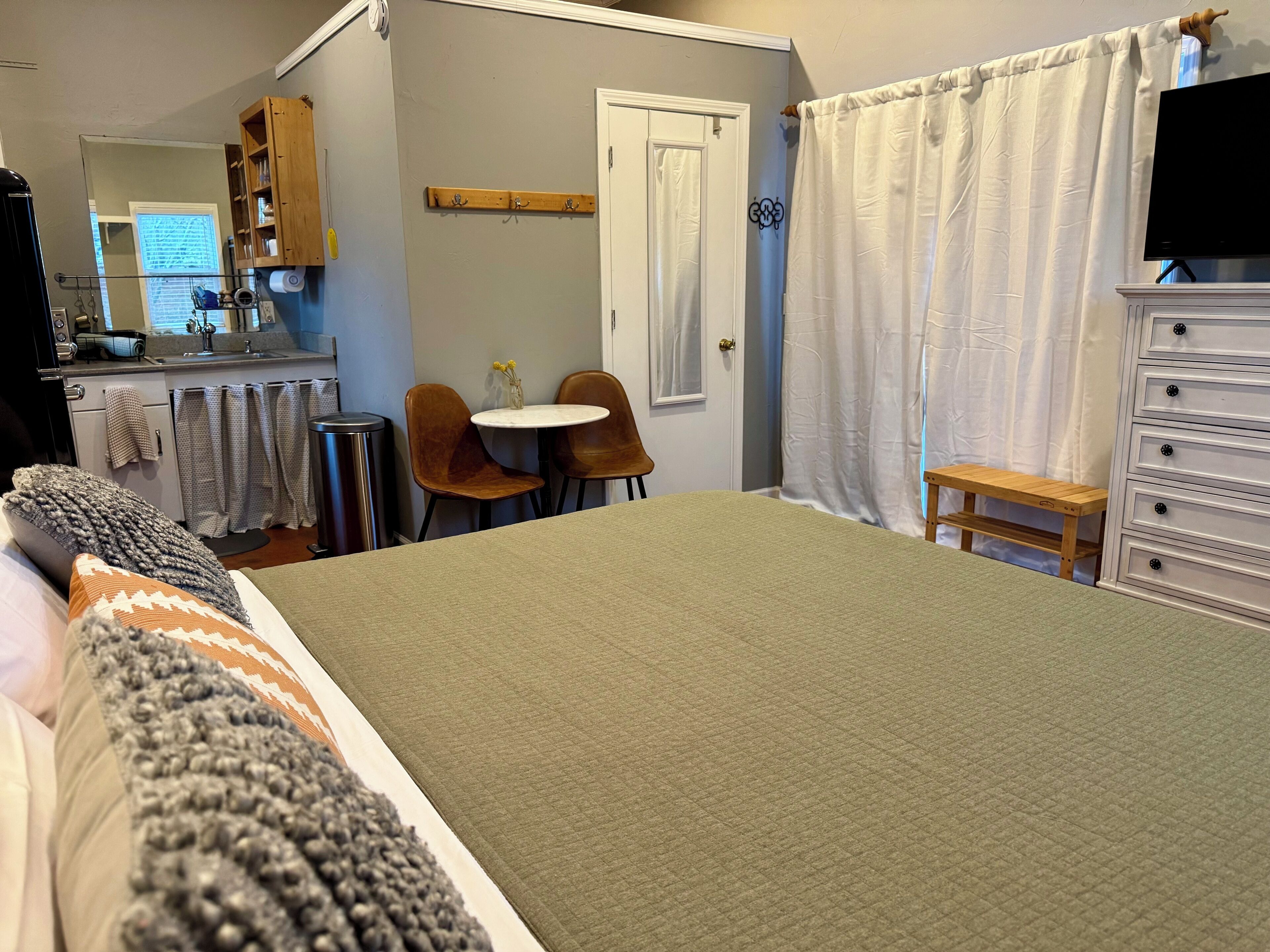 A bedroom with a bed, a small table, two chairs, a dresser, and a TV.