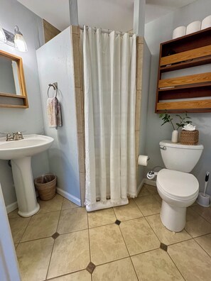 Un baño con lavamanos pedestal, inodoro y cortina de ducha.