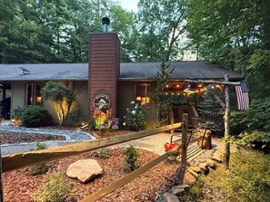 Ein Haus mit Backsteinschornstein, einer Willkommensschild, einer Veranda mit Lichterkette und einer Flagge.
