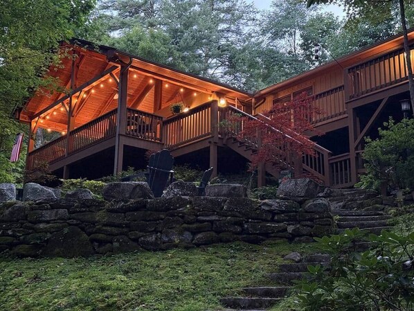 Eine Holzhütte mit überdachter Veranda und Steintreppe, umgeben von viel Grün.