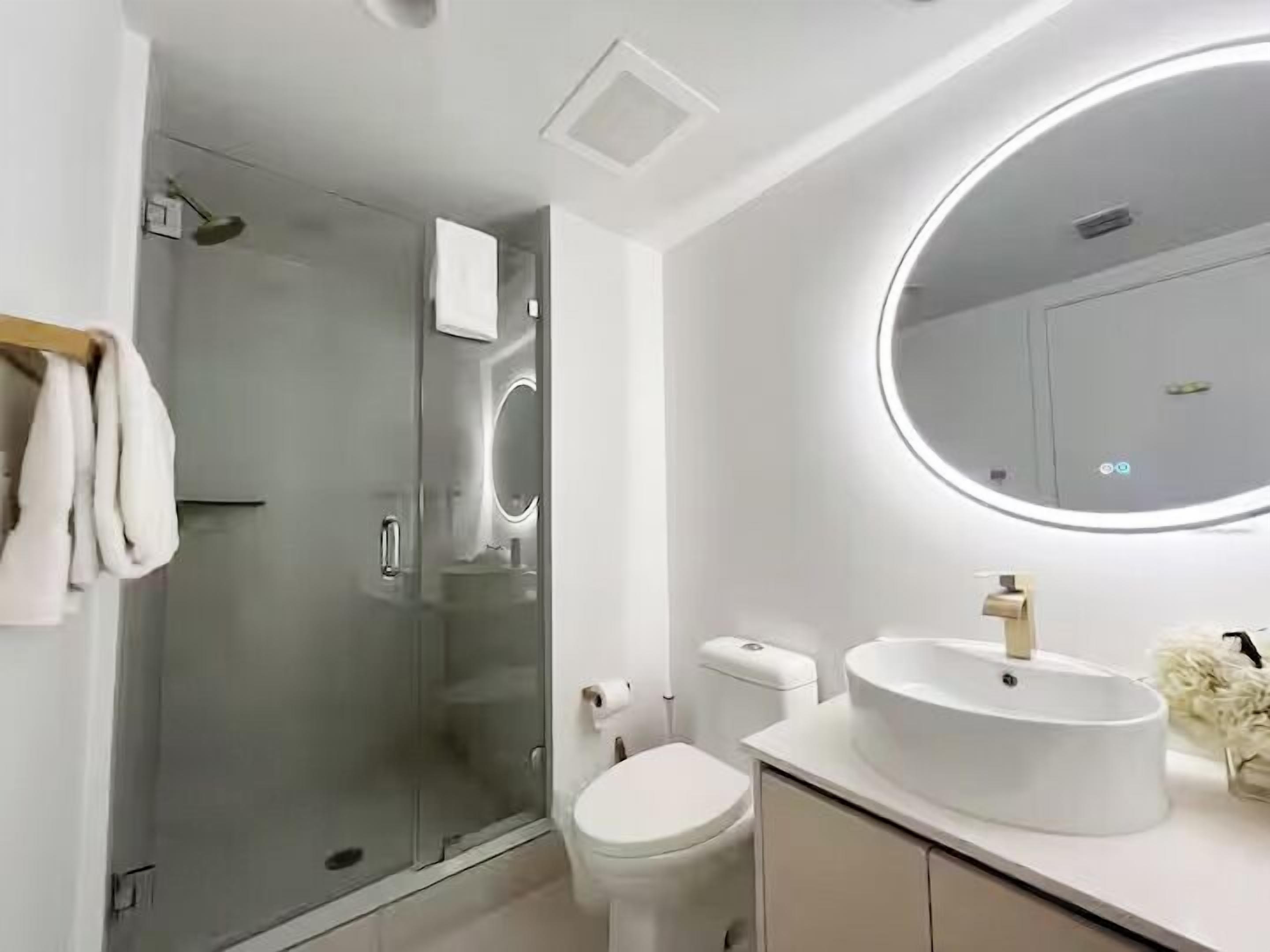 Un baño moderno con cabina de ducha de vidrio, inodoro, lavamanos con espejo y perchero.