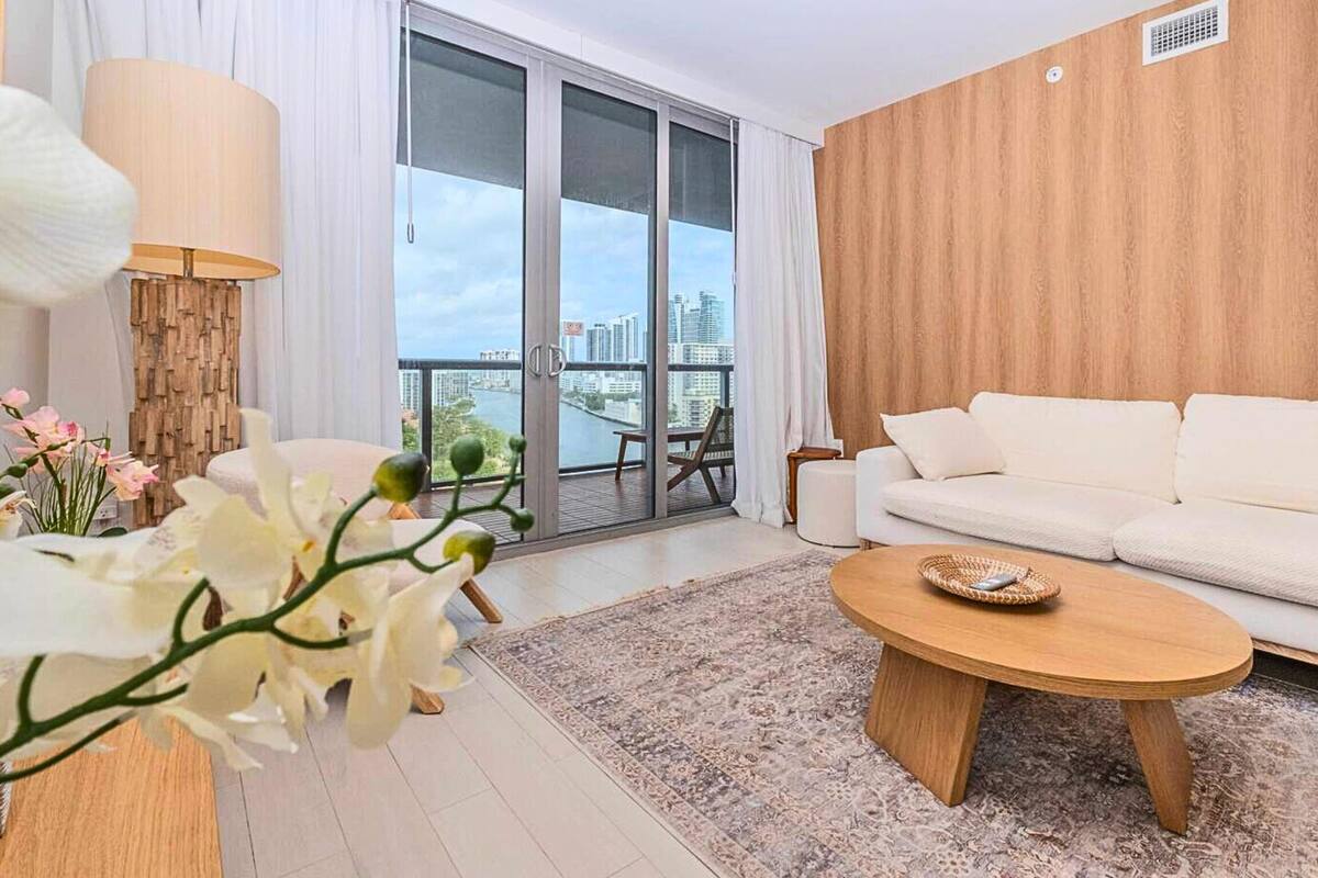 Un salon moderne avec un canapé blanc, une table basse en bois et une grande fenêtre donnant sur la ville.