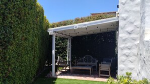 Un patio techado con techo blanco, una mesa pequeña y dos sillas.