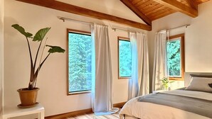 A bedroom with a bed, a potted plant, and three windows with curtains.