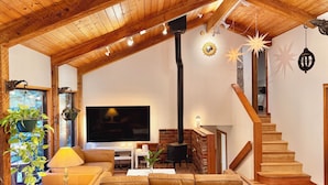 A cozy living room with a wooden ceiling, a fireplace, a TV, and a staircase.
