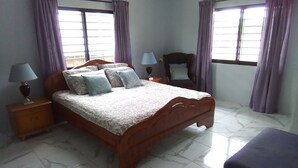 Een slaapkamer met een houten bed, twee nachtkastjes, een stoel en een bankje.