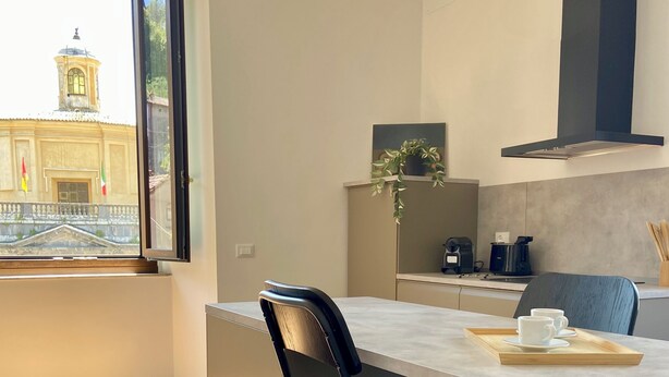 A modern kitchen with a dining area, a view of a building with a tower, and a window. - Santa Cristina Suites Balcony with a View (Bolsena)