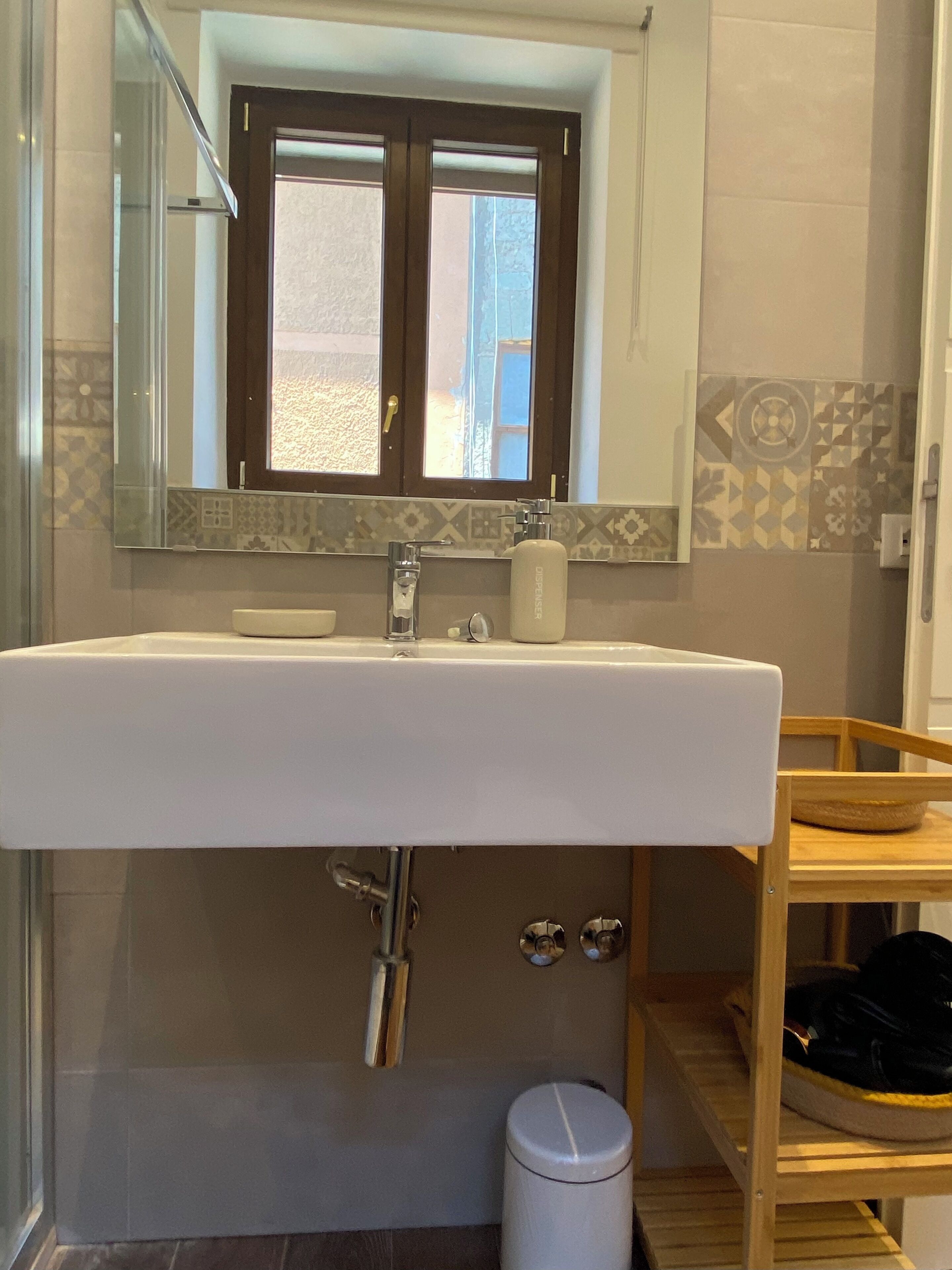 Een badkamer met een witte wastafel, een spiegel erboven en een raam met uitzicht.
