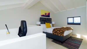 A modern bedroom with a desk, a bed with a patterned blanket, a headboard, and a window. - Bukkie’s loft place (Sandton)
