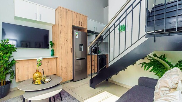 A modern kitchen with a built-in refrigerator, wooden cabinets, and a dining area with a round table and chairs. - Bukkie’s loft place (Sandton)