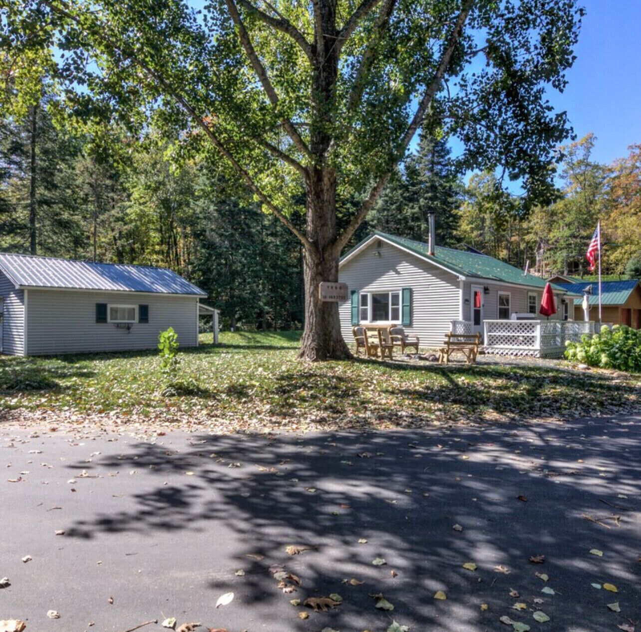 A cabin with a green roof, a porch with chairs, and a flag.