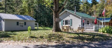 A cabin with a green roof, a porch with chairs, and a flag.