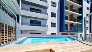 A modern building with a swimming pool and wooden deck seating. - Luxurious capetown apartment (Cape Town)