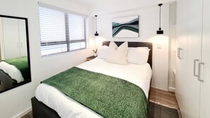 A modern bedroom with a large bed, a mirror, a window with blinds, and a painting on the wall. - Luxurious capetown apartment (Cape Town)