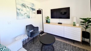 A modern living room with a grey sofa, a black armchair, a round coffee table, a flat-screen TV, a white cabinet, and a painting on the wall. - Luxurious capetown apartment (Cape Town)