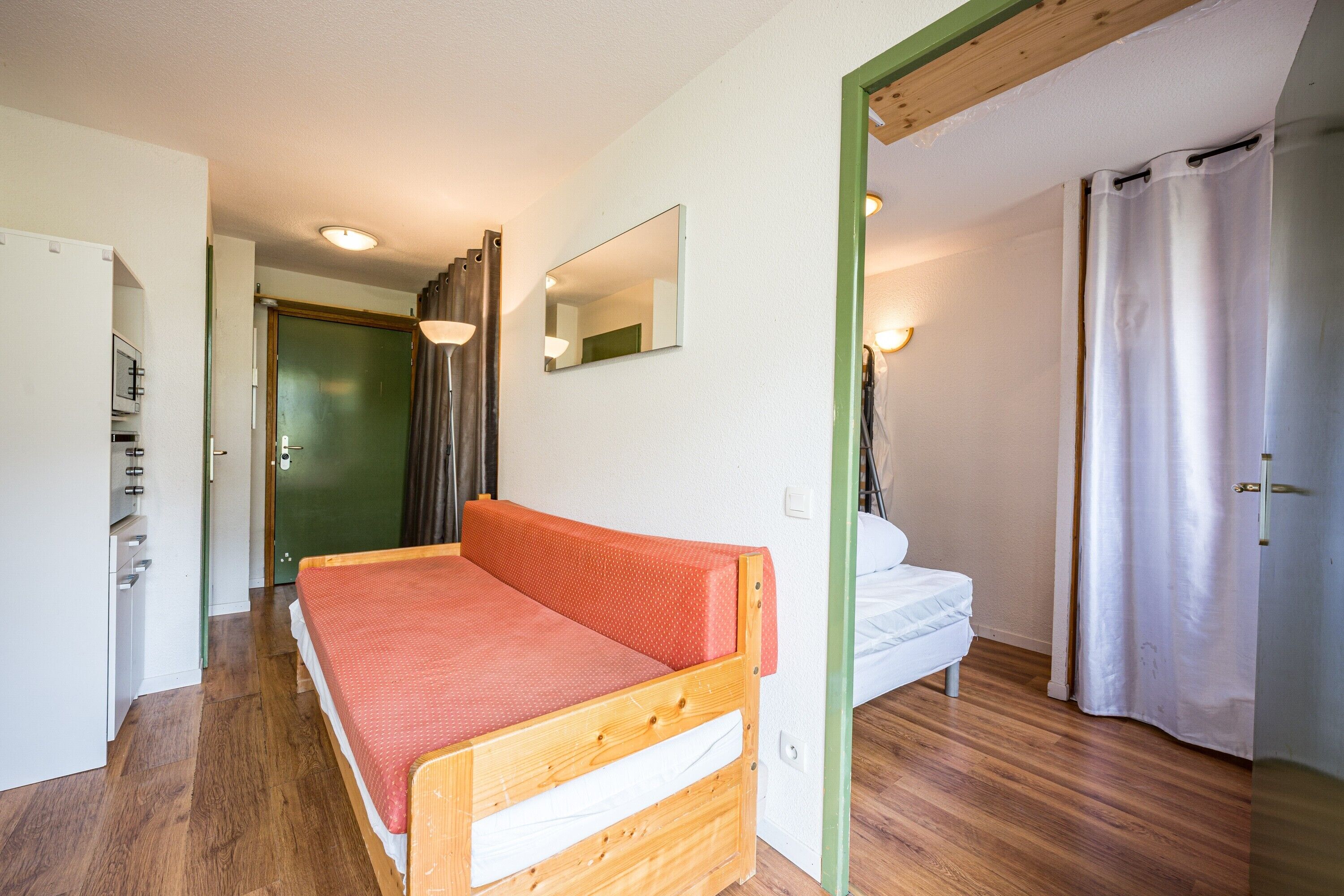 A room with a wooden bed, a white sofa, a mirror, and a green-framed door.
